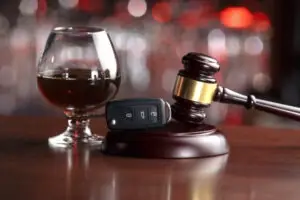 A glass of red wine and car keys pictured next to a gavel.