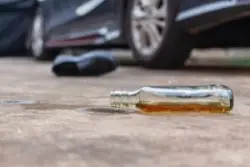 bottle of alcohol on ground next to car