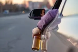 man holding beer bottle outside of the car while driving