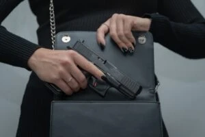 Woman holds a gun over the open main pocket of her purse as she wonders, “Can a felon own a gun in Ohio?”
