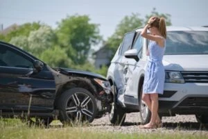 A driver standing next to her damaged car, wondering if she should get a lawyer for a minor car accident.