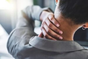 A woman holding her neck after an injury, wondering what the average settlement is for a neck and back injury.