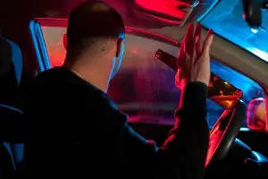 motorist holding beer bottle looks back at police lights