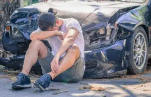 a guy sitting in front of a wrecked car