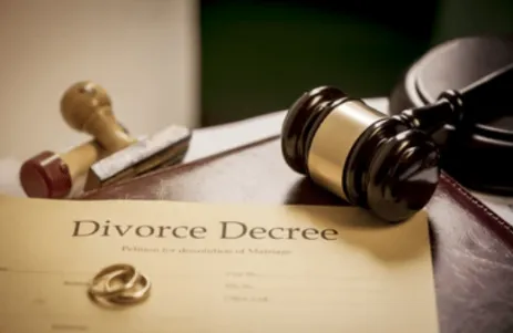 A paper that reads "Divorce Decree," two gold bands, rubber stamps, and a wooden gavel lay on top of it.