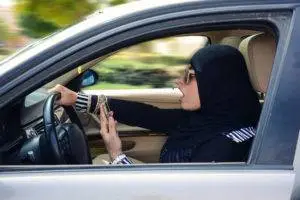 A woman driving quickly while holding a cell phone.