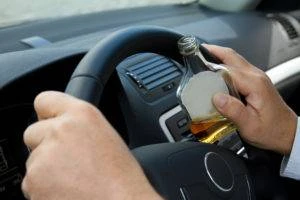 hands on steering wheel holding bottle of liquor