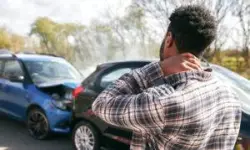 man rubbing neck beside crashed cars