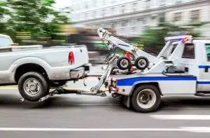 tow truck speeding down road with broken down vehicle in tow