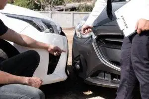 An insurance adjuster inspects damages on cars with a car accident victim.