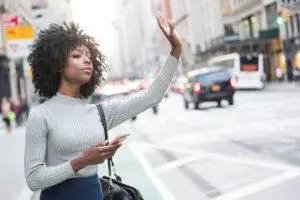 a woman holding a cellphone and flagging down her rideshare driver