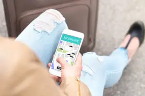 a woman sitting with her luggage and looking at the rideshare app on her phone