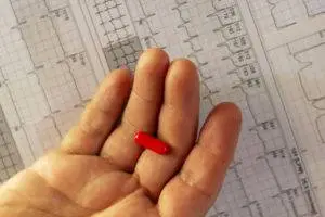 red pill in hand above medical charts