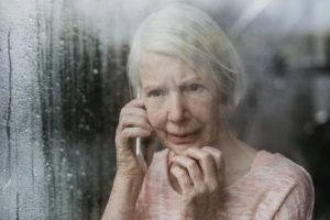 senior woman looks worriedly out window while on phone