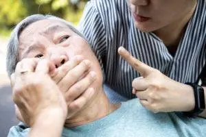 woman covering mouth of senior citizen with angry gesture