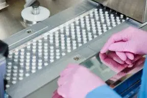 worker inspecting pill packages on conveyor belt