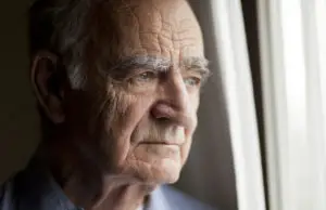worried elderly man peers out window