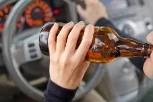 closeup of driver drinking beer with one hand on wheel