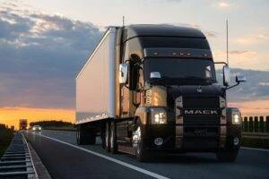 A semi-truck driving on a highway at sunset.