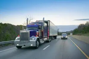 An 18-wheeler driving next to a small car. 18-wheelers can easily crush a smaller vehicle if they cause an accident.