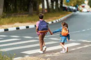 Two children hold hands while crossing the road.