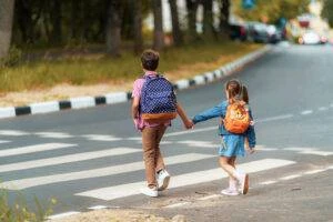 Two children hold hands while crossing the road.