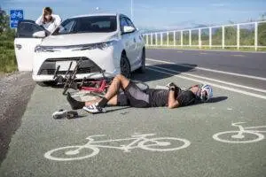 A cyclist lying in a bike lane after they’ve been hit by a car with the driver looking on. This rider needs the help of our O’Fallon bicycle accident lawyers.