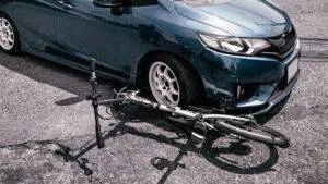 A bicycle crushed under the front of a car. If someone was riding this bike, they’d need a bicycle accident lawyer right away.