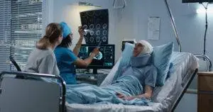 A doctor examines brain scan print-outs next to a person with an injured head lying in a hospital bed.