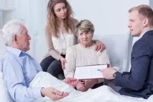 A mature man in a hospital bed is visited by female family members and a male lawyer.