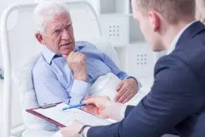 a lawyer presenting paperwork to a mature man in a hospital bed