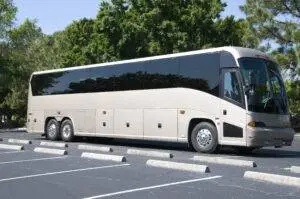 A new white bus waits in a parking lot for passengers.