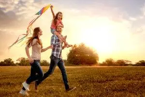 Two parents and a child fly a kite in a field after an accident.