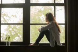 A woman sits on a windowsill and grieves a loved one.
