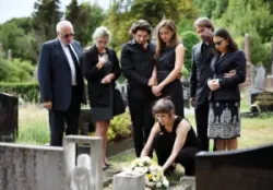 A family of seven, dressed in black, places white flowers on a loved one’s grave.