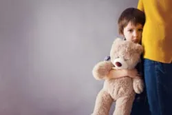 A grieving child holds his teddy bear while clinging to his mother’s leg. A Long Beach wrongful death lawyer can help you after the death of a loved one.