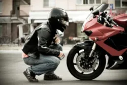 A motorcyclist kneels and examines the front of their red bike after a crash.
