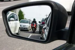 A motorist watches a motorcyclist approach in their side mirror.
