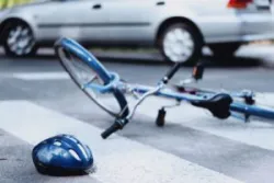 A helmet and a damaged bicycle lie on the road as a car drives off. A San Jose bicycle accident lawyer can help you hold the at-fault driver accountable.