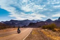 A motorcyclist in an arid landscape drives down an empty interstate.