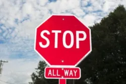 The photo depicts a four-way stop sign. Who has the right of way at a four-way stop?