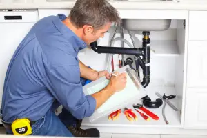 plumber performing maintenance check on kitchen sink pipes