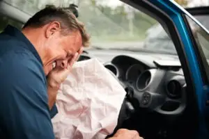 A man is in pain after the airbag deploys during a car accident.