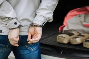 a man in handcuffs by a trunk filled with drugs
