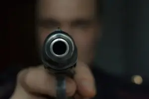 a man holds a gun aimed at the camera