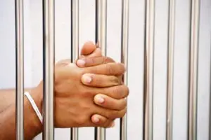 hands of a prisoner holding a bar in a jail cell