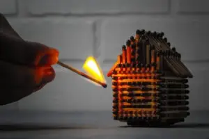 hand holding lit match to matchstick house