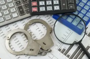 handcuffs magnifying glass and calculators on spreadsheet with data