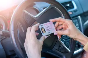 A woman holds her driver’s license inside her car.