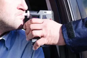 officer holds breathalyzer for motorist sitting in driver’s seat